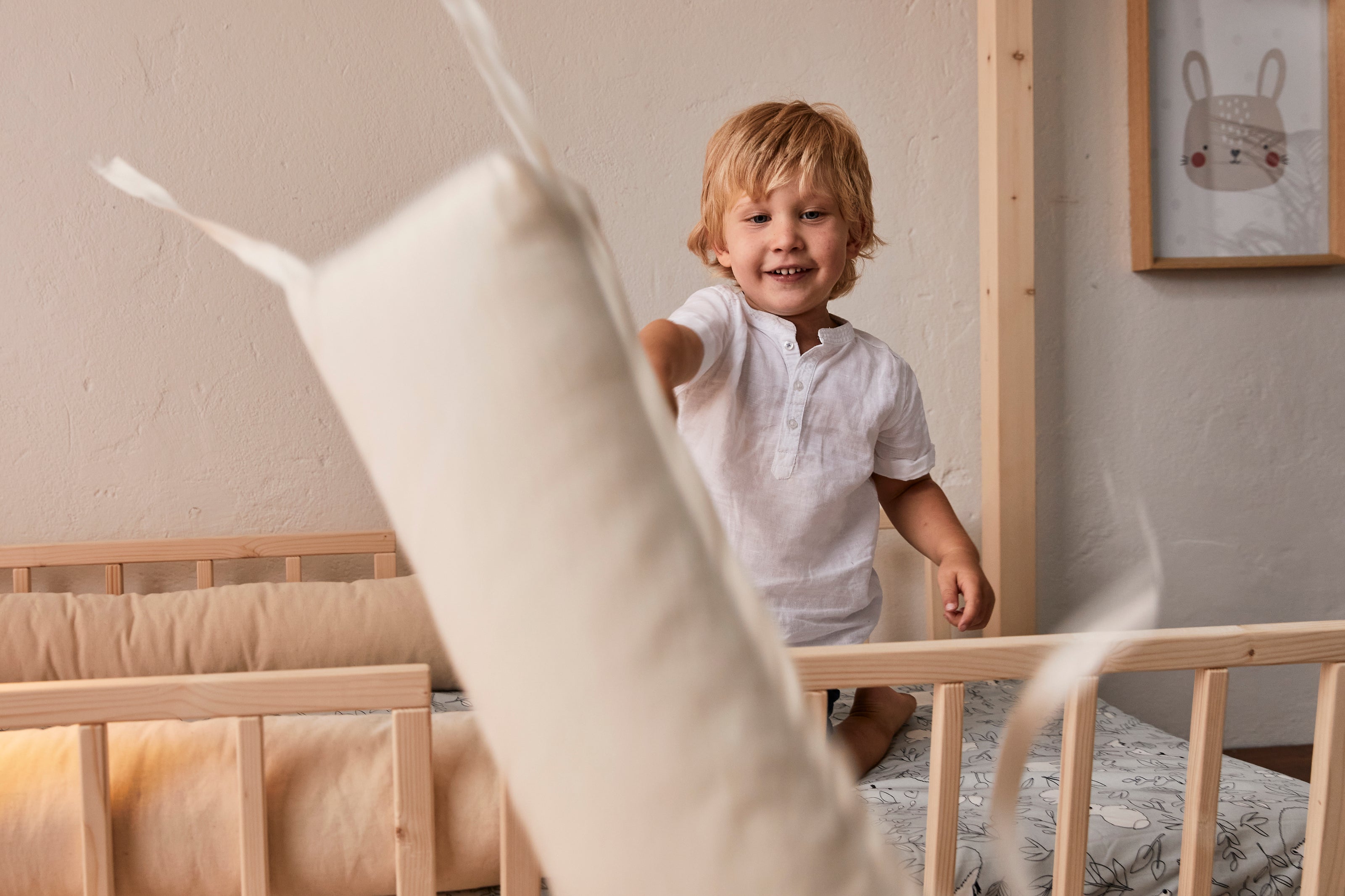 Bambino su lettino montessori con barriere in legno gioca con cuscini