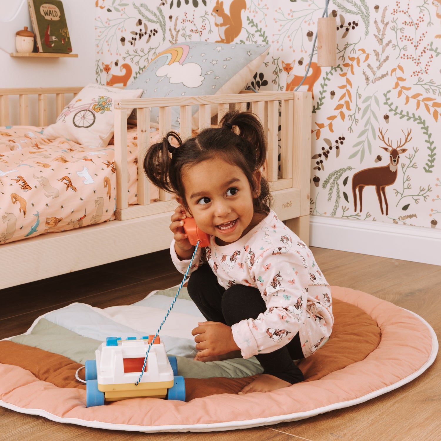 Una bambina sorridente in una cameretta nabè gioca a fare una telefonata con un apparecchio giocattolo. 