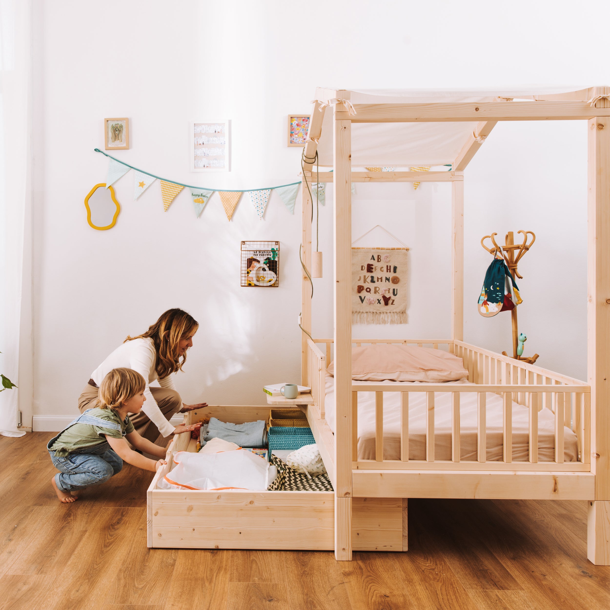 mamma e bambino aprono cassetto contenitore per letto montessori in legno naturale con baldacchino